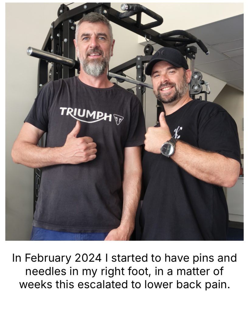 Two men stand in a gym next to a weight machine, smiling and giving a thumbs-up.